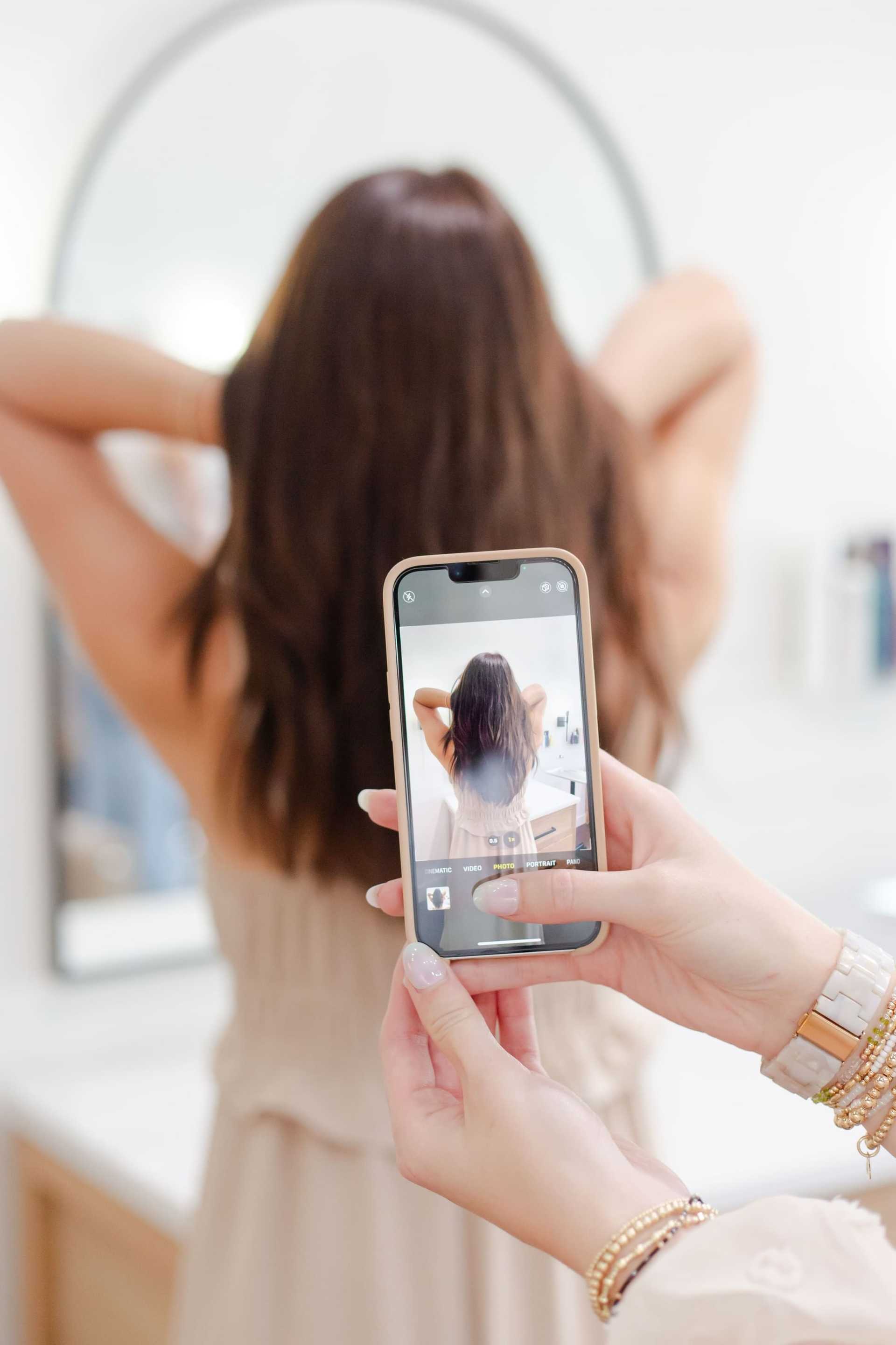 Person taking a photo of their long hair in a mirror with a smartphone.