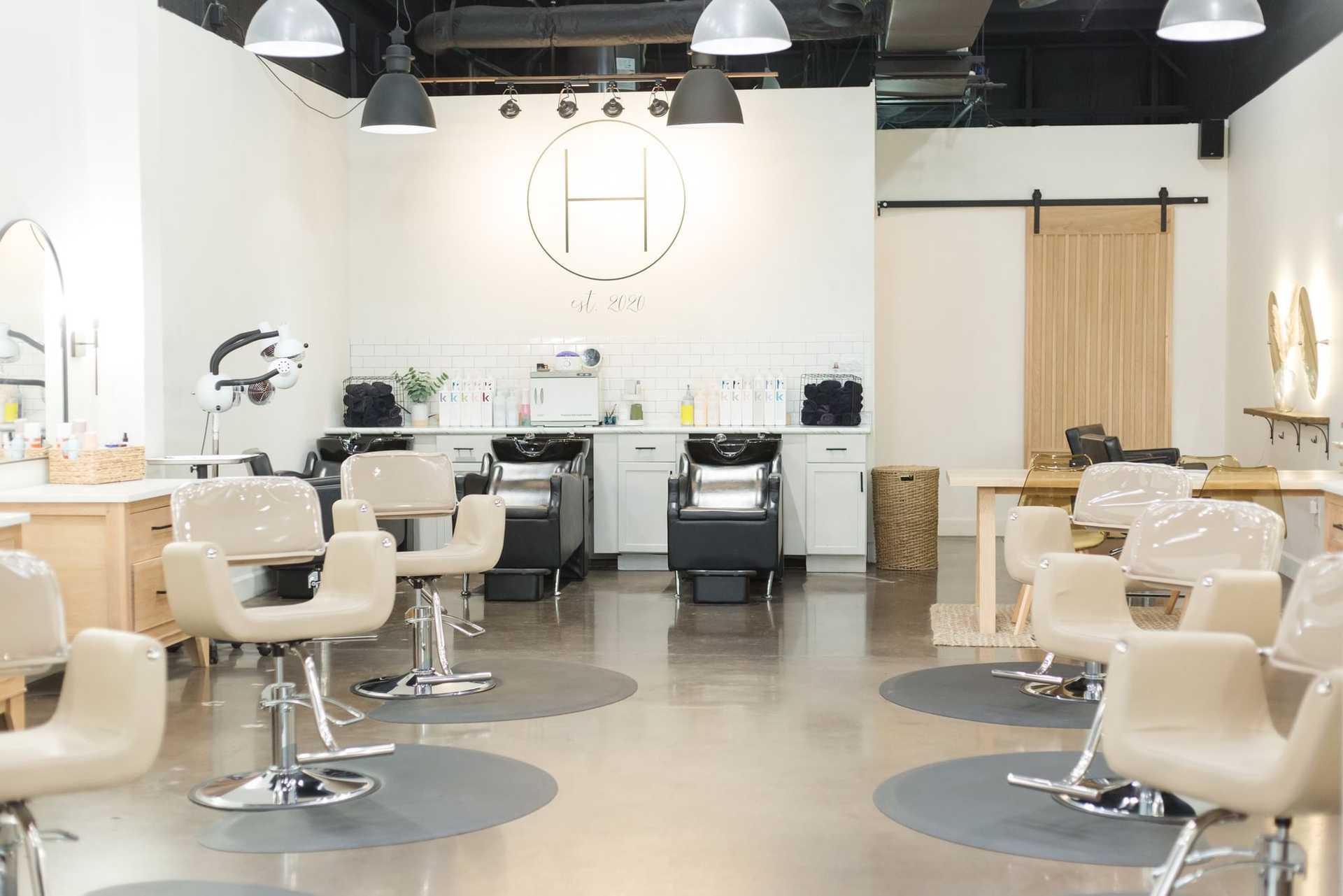 Modern hair salon with styling chairs, mirrors, and washing stations in a minimalist design.